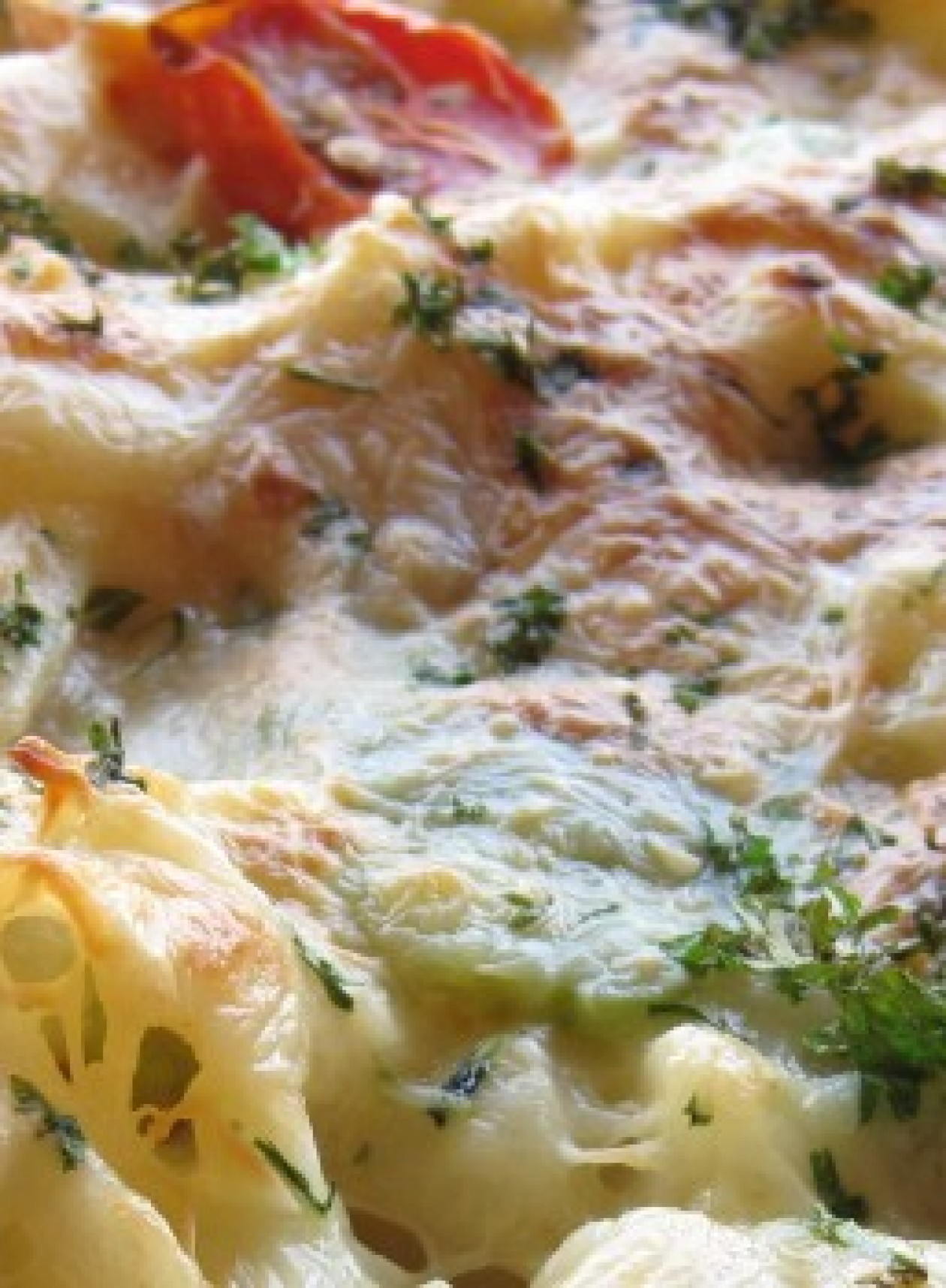 Close-up of a cheesy baked pasta dish with roasted tomato pieces and sprinkled herbs, soft focus, warm creamy colors